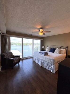 Ein Schlafzimmer mit Bett, Stuhl, Deckenventilator und großem Fenster mit Blick auf das Wasser.
