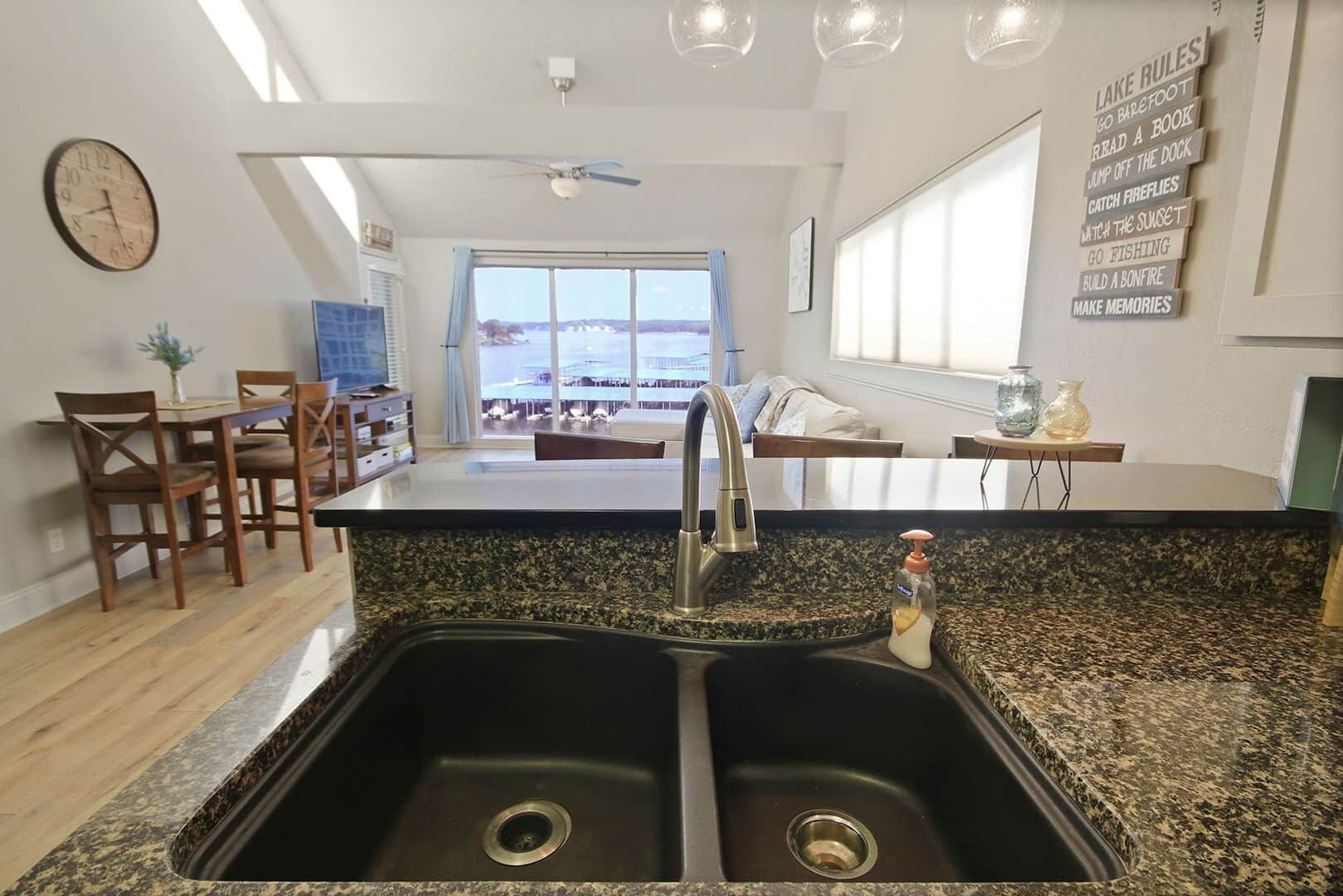 Una cocina con un lavamanos doble, sillas de madera, una mesa de comedor y vista al agua.