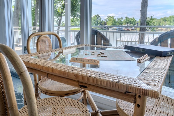 A glass-top table with Scrabble tiles, wicker chairs, and a view of a lake. - Your Perfect LOZ Getaway! (Pawhuska Township)