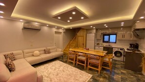 A modern living room with a sofa, a dining table, and a kitchen area with appliances. - Kent Villas Heated Pool Villas (Demre)