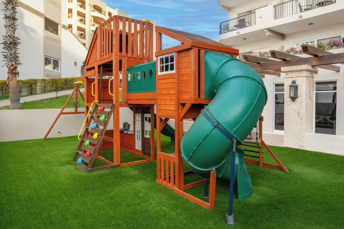 A wooden play structure with a slide and climbing ladder, surrounded by artificial grass.