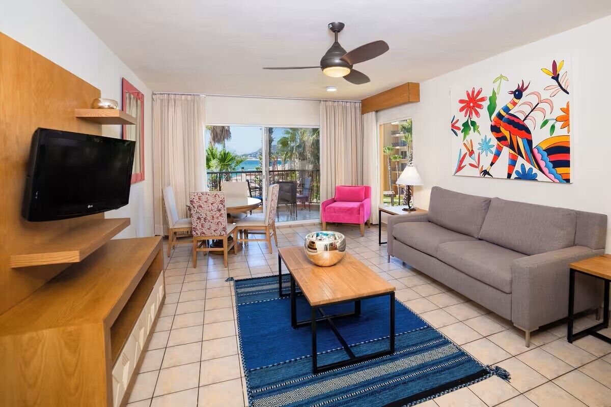 Ein Wohnzimmer mit Flachbildfernseher, Deckenventilator, Sofa, Couchtisch und einem farbenfrohen Wandbild.