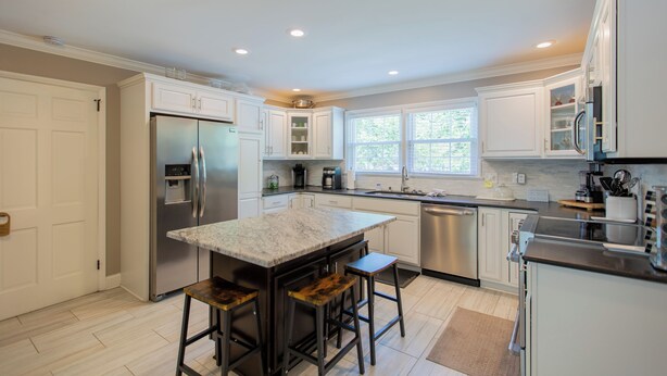 A modern kitchen with a central island, stainless steel appliances, and white cabinetry. - Spacious 6BR w/ Firepit, Porch, Prime Location (High Point)