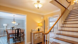 A staircase with wooden steps and white railings, a dining area with a wooden table and chairs, and a ceiling light fixture. - Spacious 6BR w/ Firepit, Porch, Prime Location (High Point)