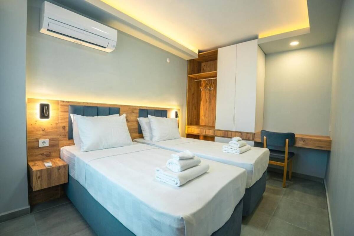 A hotel room with two beds, a desk, a wardrobe, and an air conditioning unit.