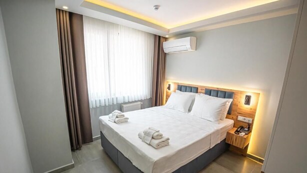 A modern hotel room with a large bed, a bedside table with a lamp, and an air conditioning unit on the wall. - Airport Bayrak Residences Trabzon (Trabzon)