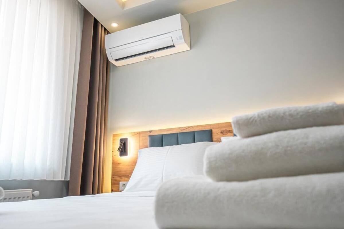 A hotel room with a bed, white towels, an air conditioning unit, and a nightstand with a lamp.