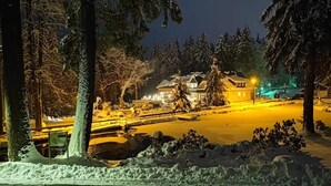A snow-covered landscape with a building illuminated by warm lights, surrounded by trees. - Apartment in A Hotel 'Pensionszimmer 24 Qm Mit Balkon (copy)' with Shared Garden, Balcony and Wi-Fi (Suhl)