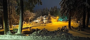Un paisaje nevado con un edificio iluminado por luces cálidas, rodeado de árboles.