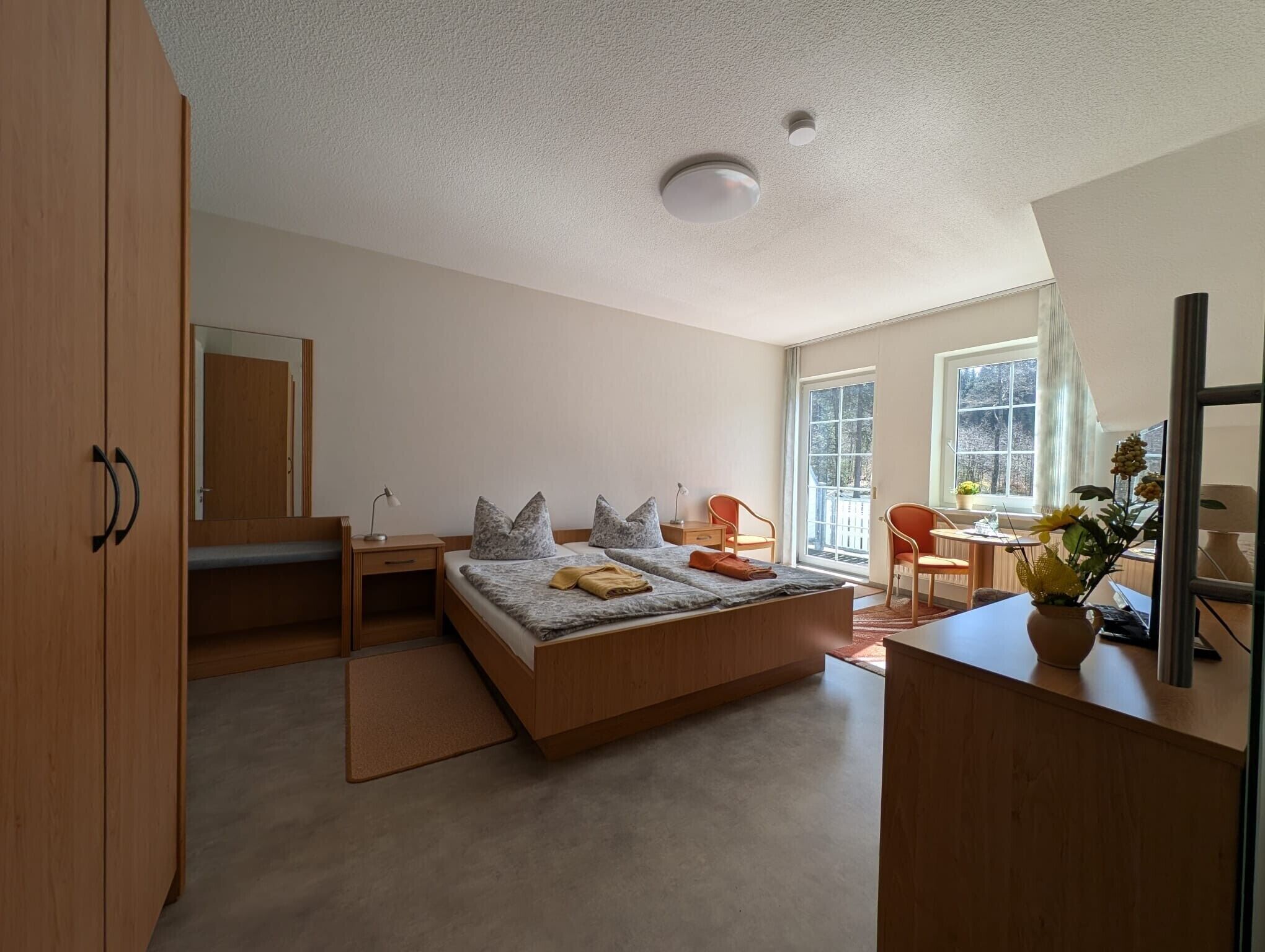 Ein Schlafzimmer mit Bett, Nachttisch, Lampe, Stuhl, Schreibtisch und einem Fenster mit Blick.