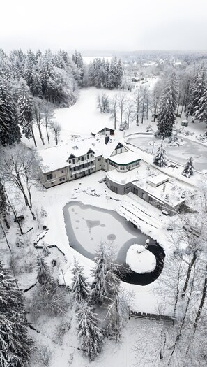 A snow-covered landscape with a large building complex, including multiple structures and a pond.