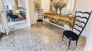 Una habitación con suelo de mármol, una silla negra, una consola dorada ornamentada y un espejo grande.