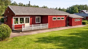A red building with a white fence, a grassy lawn, and trees in the background. - Central house with AC near the beach (Piteå)