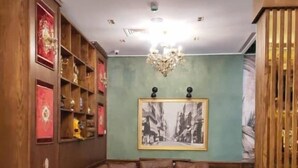A room with a brown leather sofa, a round table, wooden shelves, and a chandelier. - L amiral (Oran)