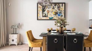 Ein Essbereich mit einem schwarzen Tisch, goldenen Stühlen und einem gerahmten abstrakten Gemälde an der Wand.