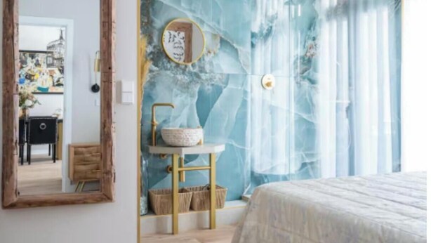 Ein Schlafzimmer mit Marmorwand, einem runden Spiegel, einem Nachttisch mit einer Schale und einem Bett.