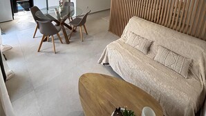 A modern living space with a sofa, dining table, chairs, kitchen area, and a TV. - Mazet Léa - Quiet terrace & pool (Le Rouret)