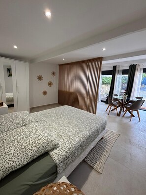 A modern bedroom with a large bed, a wardrobe, a dining area with chairs, and a view through the window. - Mazet Léa - Quiet terrace & pool (Le Rouret)