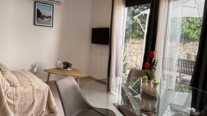 A modern living room with a glass dining table, two chairs, a sofa, a TV, and a window with curtains. - Mazet Léa - Quiet terrace & pool (Le Rouret)