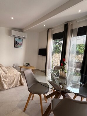 A modern living room with a glass dining table, two chairs, a sofa, a TV, and a window with curtains. - Mazet Léa - Quiet terrace & pool (Le Rouret)