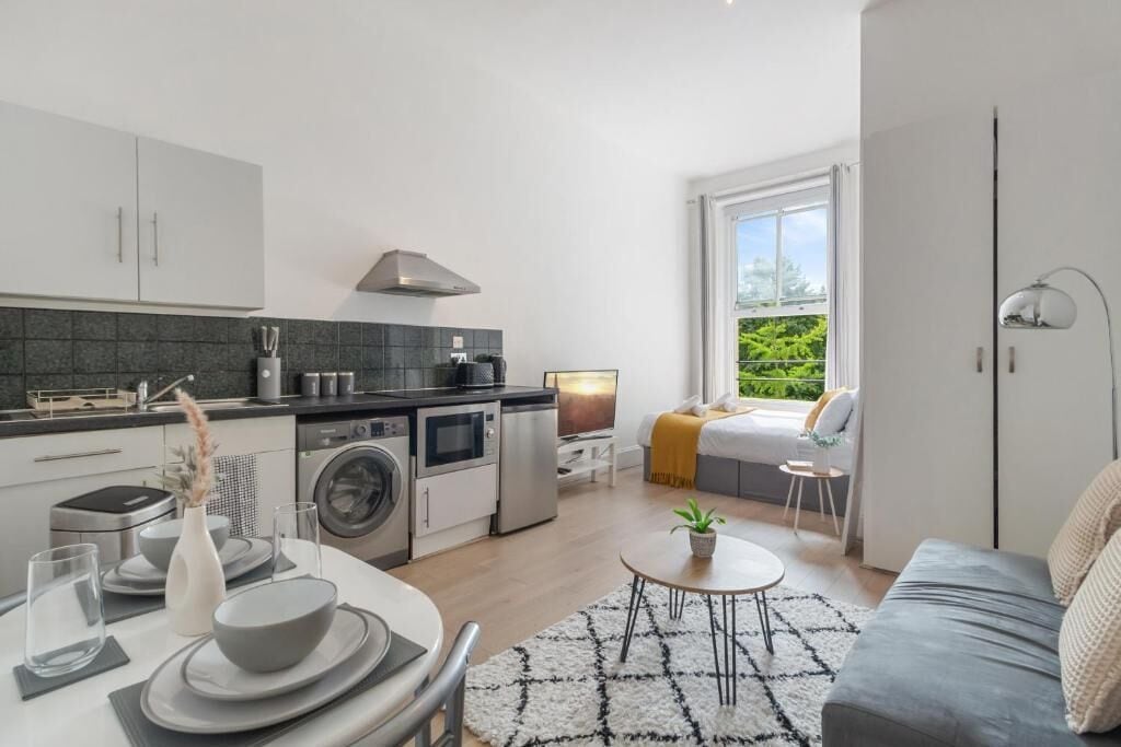 Un espacio habitable compacto con kitchenette, comedor, sofá y ventana con vista a vegetación.