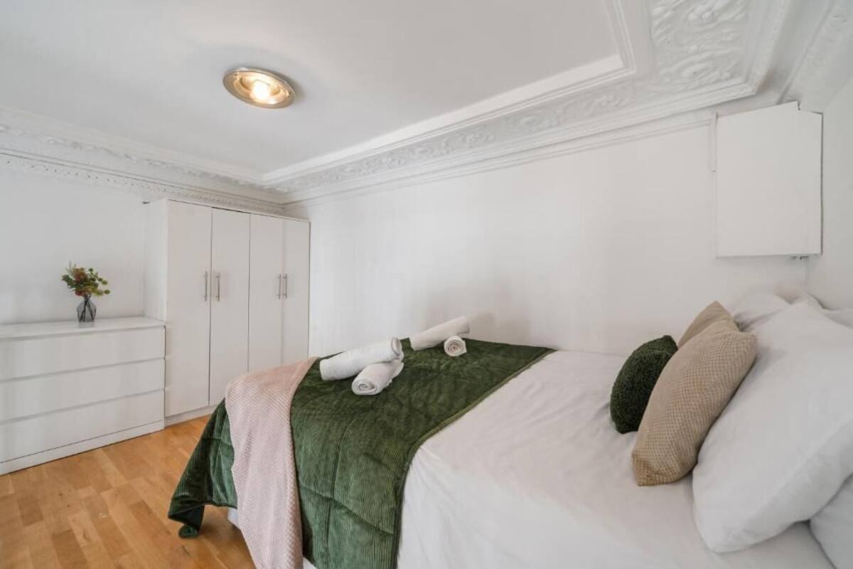 A bedroom with a bed, pillows, a green blanket, a white wardrobe, and a small plant.