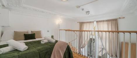 Et soveværelse med seng, en balkon med gelænder og en trappe.