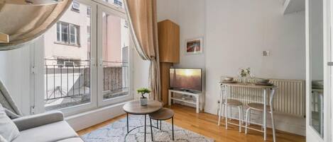 Un salon moderne comprenant un canapé, un téléviseur, une petite table avec une plante et un coin repas avec des chaises.