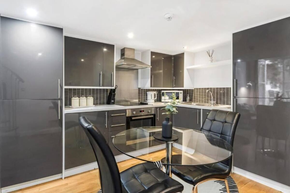 A modern kitchen with dark cabinets, a glass dining table, and black chairs.