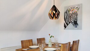 Una mesa de comedor con sillas, un florero con flores y un cuadro de una cebra en la pared.