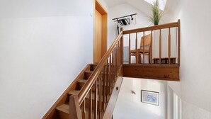 Una escalera con barandillas de madera, una silla, un radiador y un cuadro en la pared.