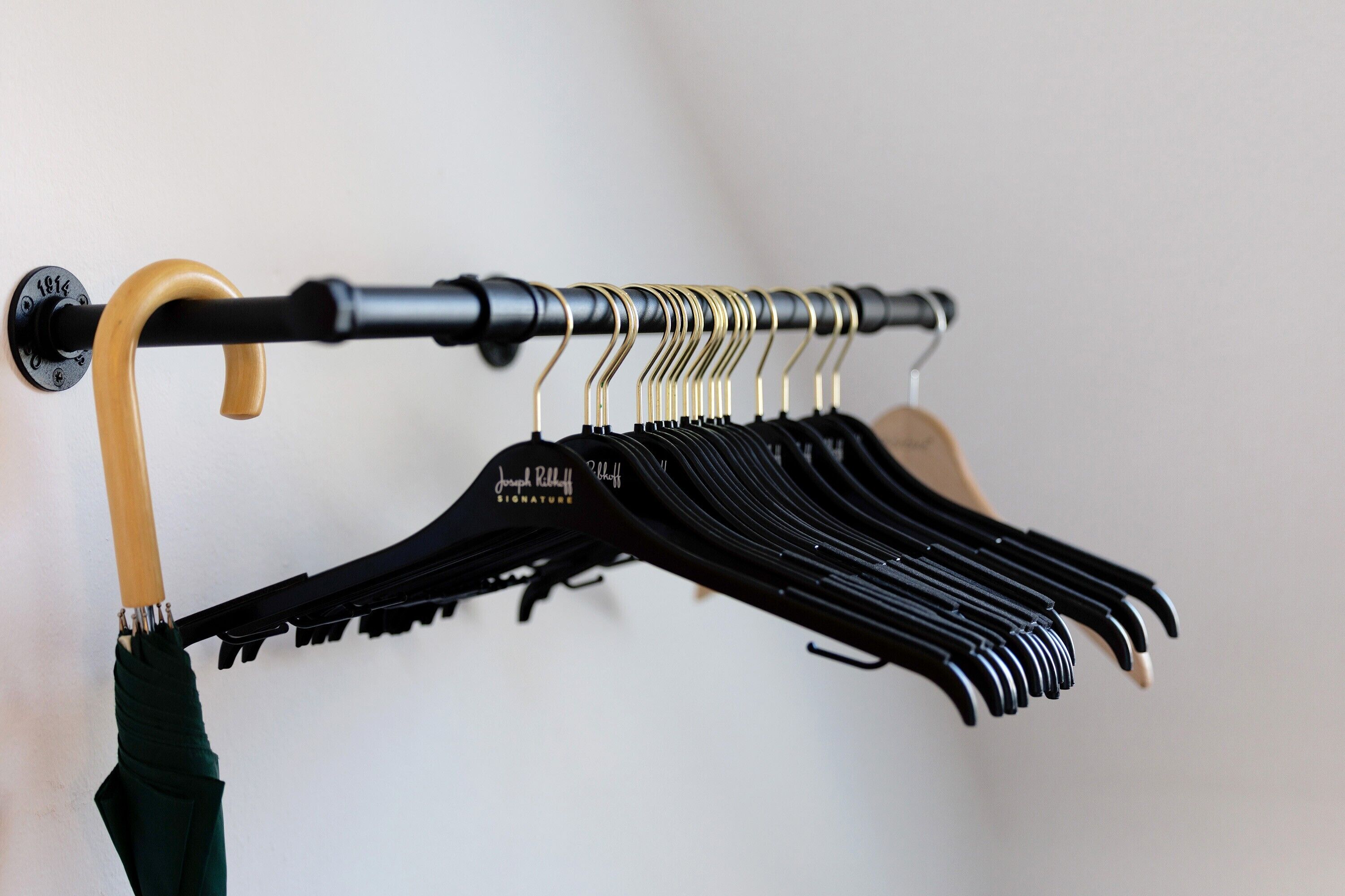 Un porte-manteau mural doté de plusieurs crochets et d’un parapluie à manche en bois.