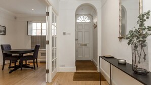 Un pasillo con comedor, una puerta con panel de vidrio y una consola con un florero.