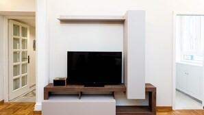 Ett modernt vardagsrum med en platt-TV placerad på ett träställ, ett vitt skåp och en dörr med frostade glaspaneler.