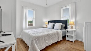 Une chambre à coucher comprenant un lit, des tables de chevet, un ventilateur de plafond et une fenêtre avec des stores.