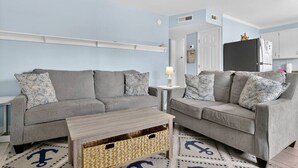 Un salon avec deux canapés gris, une petite table basse en bois et un tapis à motifs.