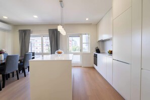 A modern kitchen with white cabinets, a central island, and a dining area with chairs and a table. - Modern & Spacious Flat with Balcony by HostWise (Porto)