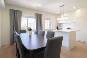 A modern kitchen with white cabinets, a central island, and a dining area with a table and chairs. - Modern & Spacious Flat with Balcony by HostWise (Porto)