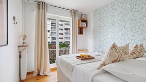 Una camera da letto con un letto, un vassoio con la colazione, una finestra con tende, una mensola a muro e vista su un edificio.