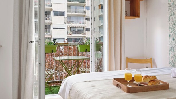 Una camera d'albergo con un letto, un vassoio per la colazione e vista su un balcone con recinzione e edifici.