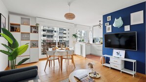 Un soggiorno moderno con zona pranzo, televisore e cucina visibile tramite un'apertura.