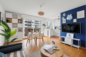 A modern living room with a dining area, a TV, and a kitchen visible through an open door. - Charming 2BR Flat Near Eiffel Tower & Invalides (Paris)