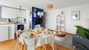Una cucina moderna con mobili bianchi, un'area pranzo con un tavolo rotondo e un soggiorno con divano e una pianta.