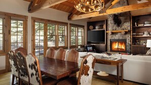 Un interior rústico con chimenea de piedra, vigas de madera y una zona de comedor con sillones de cuero.