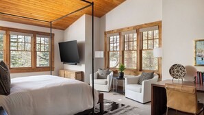 Un dormitorio con una cama, un escritorio, una silla, un televisor y ventanas amplias.