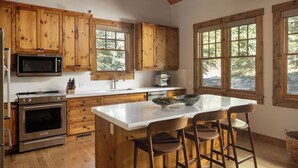 Una cocina con armarios de madera, microondas, horno, lavabo y una isla grande con taburetes de bar.