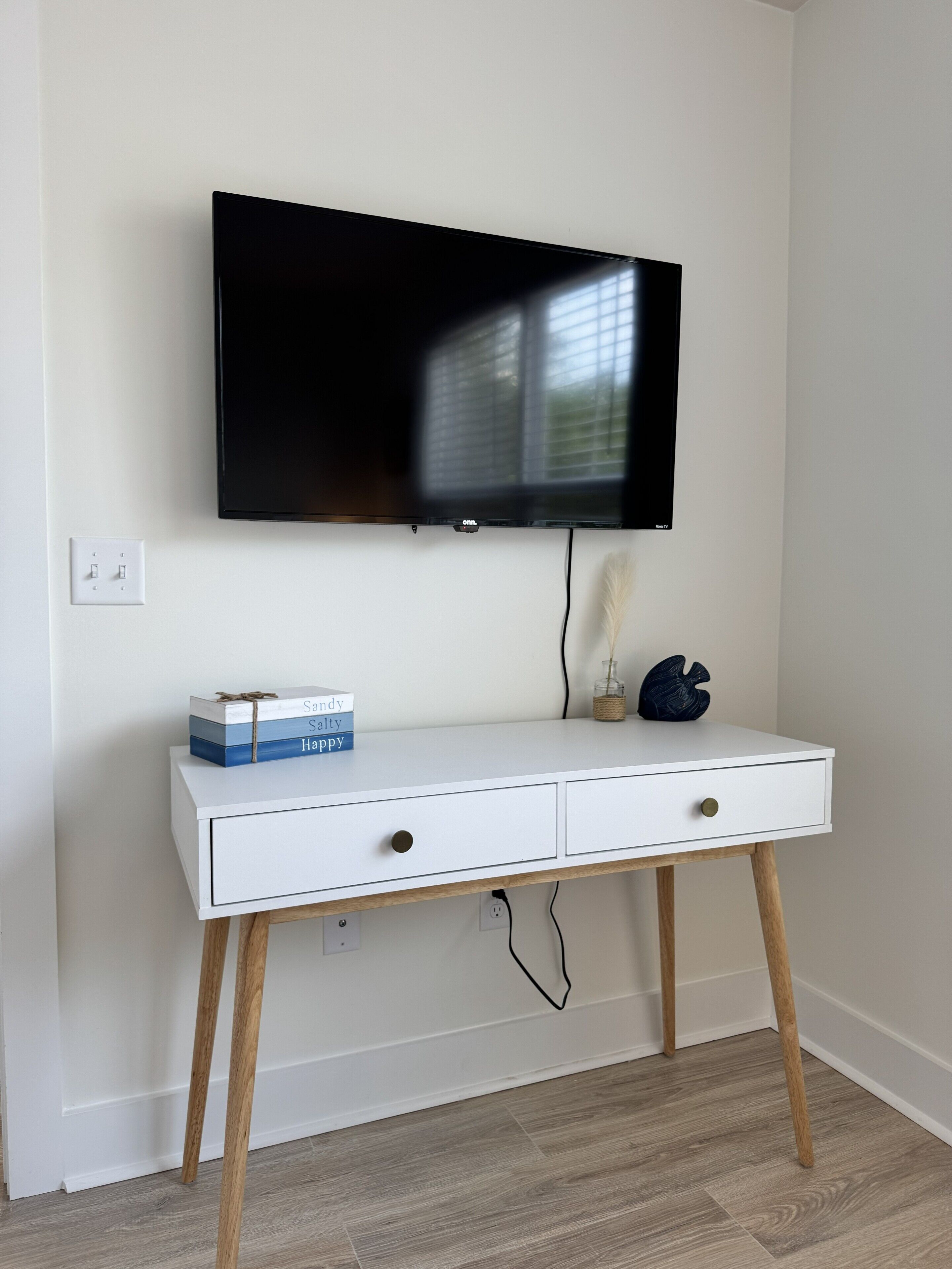 Ett vitt TV-bord med en platt-TV monterad ovanpå, en liten prydnad och en låda med böcker.