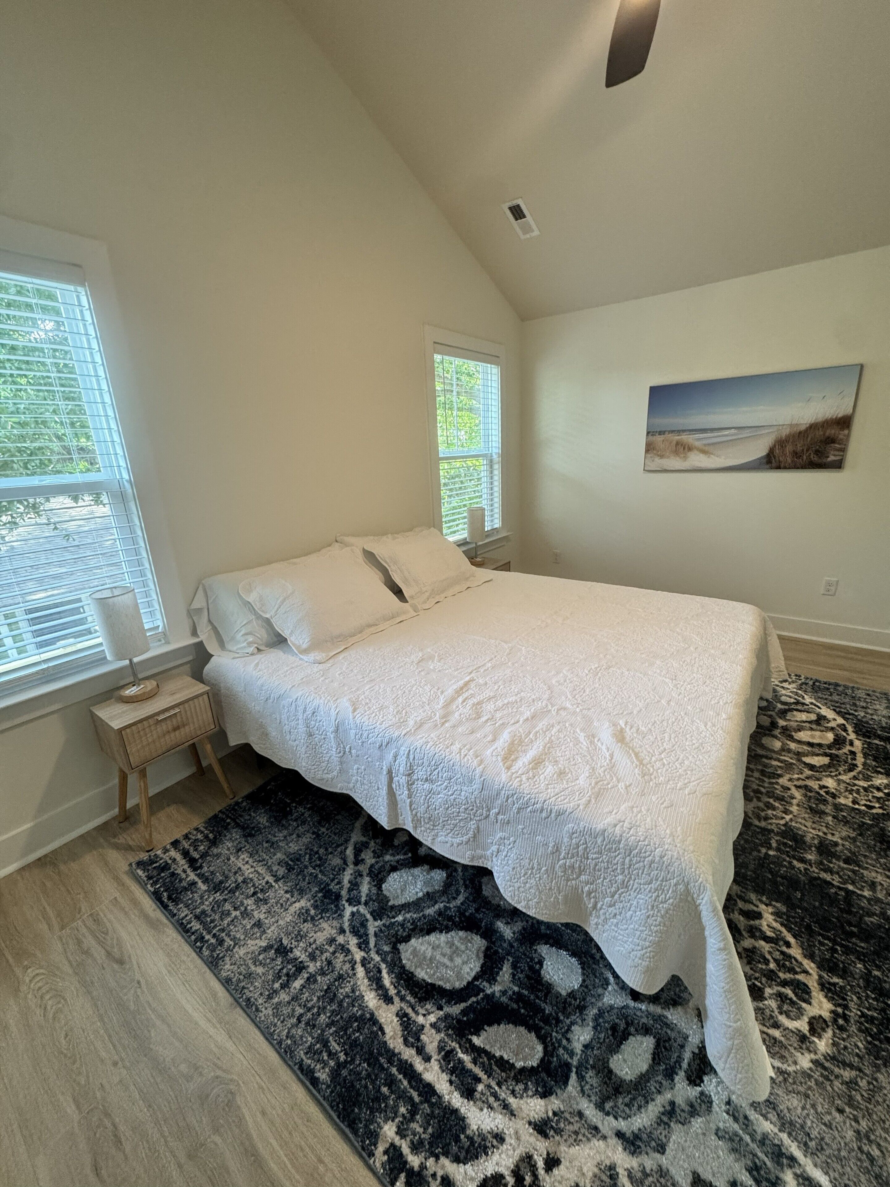 A bedroom with a bed, a nightstand, a window, and a painting on the wall.