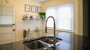 Una cocina con un lavamanos doble, grifo de acero inoxidable y una encimera con un tarro de vidrio y un hervidor.