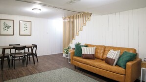Una sala de estar con un sofá de cuero marrón, una mesa de comedor de madera, sillas y una escalera.